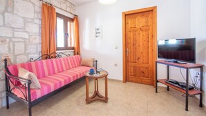 Ein Zimmer mit einer Steinswand, einem rosa gestreiften Sofa, einer Holztür und einem Fernseher auf einem Tisch.