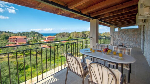 Ein Balkon mit Tisch für zwei Personen, mit Blick auf eine reizvolle Landschaft, einschließlich Häuser und Grünflächen.
