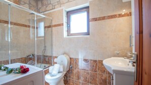 Ein Badezimmer mit Dusche, Toilette, Waschbecken und einem kleinen Fenster.