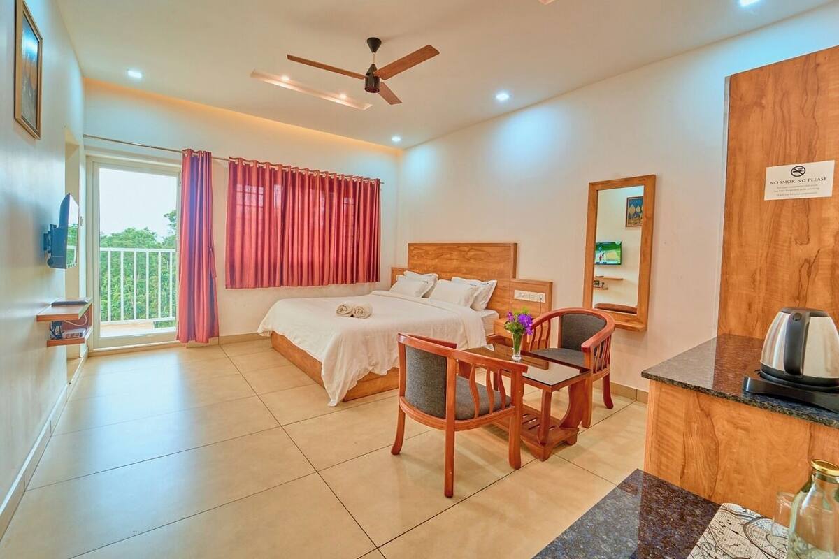 A hotel room with a bed, a desk, a chair, a ceiling fan, and a view of the outdoors.