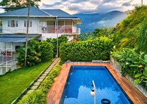 A residential property with a swimming pool, a two-story house with a balcony, and a lush garden. - Munnar Ice Pellets Resort with Pool (Devikolam)