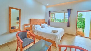 A bedroom with a bed, a chair, a table, a mirror, and a window with curtains. - Munnar Ice Pellets Resort with Pool (Devikolam)