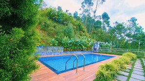 A swimming pool with metal railings, surrounded by a wooden deck and lush greenery. - Munnar Ice Pellets Resort with Pool (Devikolam)