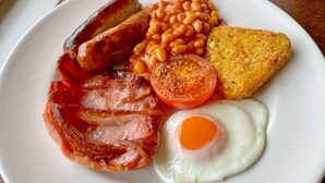 A plate of breakfast food including sausages, beans, bacon, a fried egg, a tomato, and a hash brown. - Munnar Ice Pellets Resort with Pool (Devikolam)