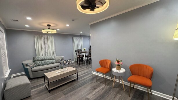 Un salon moderne comprenant un canapé, une table basse et deux fauteuils, un coin repas avec une table et des chaises, et un ventilateur de plafond.
