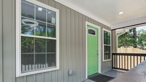 Une maison avec une façade extérieure, une porte verte, un porche couvert et une fenêtre avec des stores.