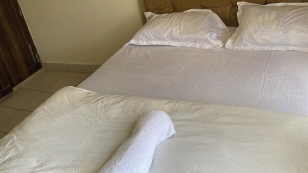 Habitación de hotel con dos camas, cabecera y una toalla blanca enrollada sobre la cama.