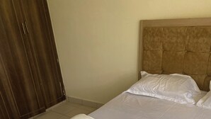 Habitación de hotel con dos camas, una puerta de madera y un cabecero color crema.