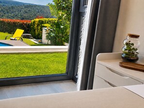 A modern room with a large window, a small table with a plant, and a view of a well-maintained garden and pool. - An oasis in Santiago, with a pool, garden, and bus to the city center (Teo)