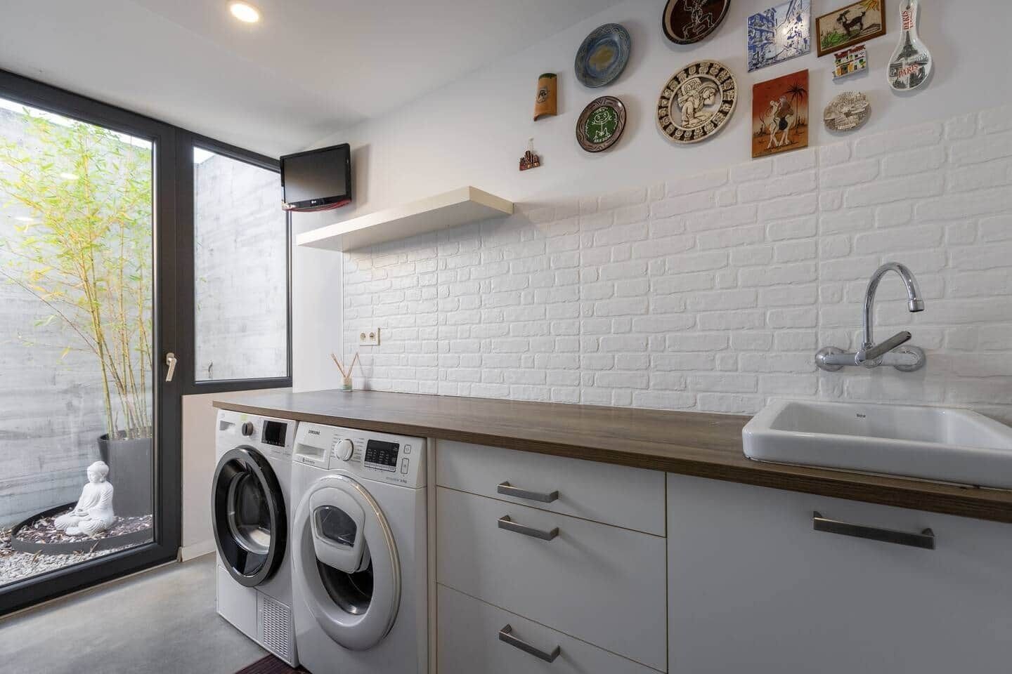 A modern laundry room with a washing machine, a sink, and decorative plates on the wall.