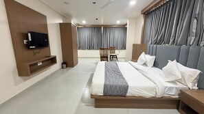 Ein modernes Hotelzimmer mit einem großen Bett, einem an der Wand befestigten Fernseher, einem kleinen Tisch und einem Sessel.