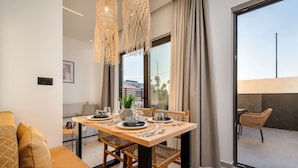 Un coin repas avec une table dressée pour deux personnes, des chaises en osier et une vue sur l’extérieur grâce à de grandes fenêtres.