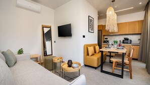 Un salon moderne comprenant un canapé, une table à manger avec des chaises, un coin cuisine et un téléviseur fixé au mur.