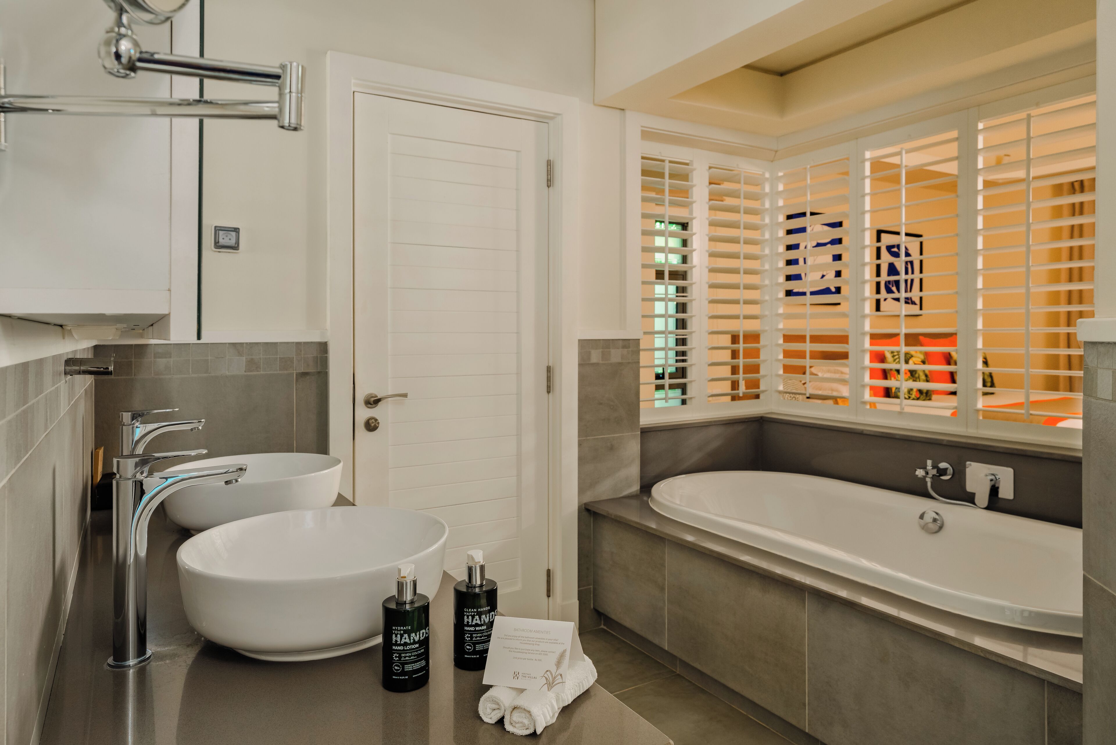 Une salle de bain moderne avec un double vasque, une baignoire et une fenêtre équipée de stores.