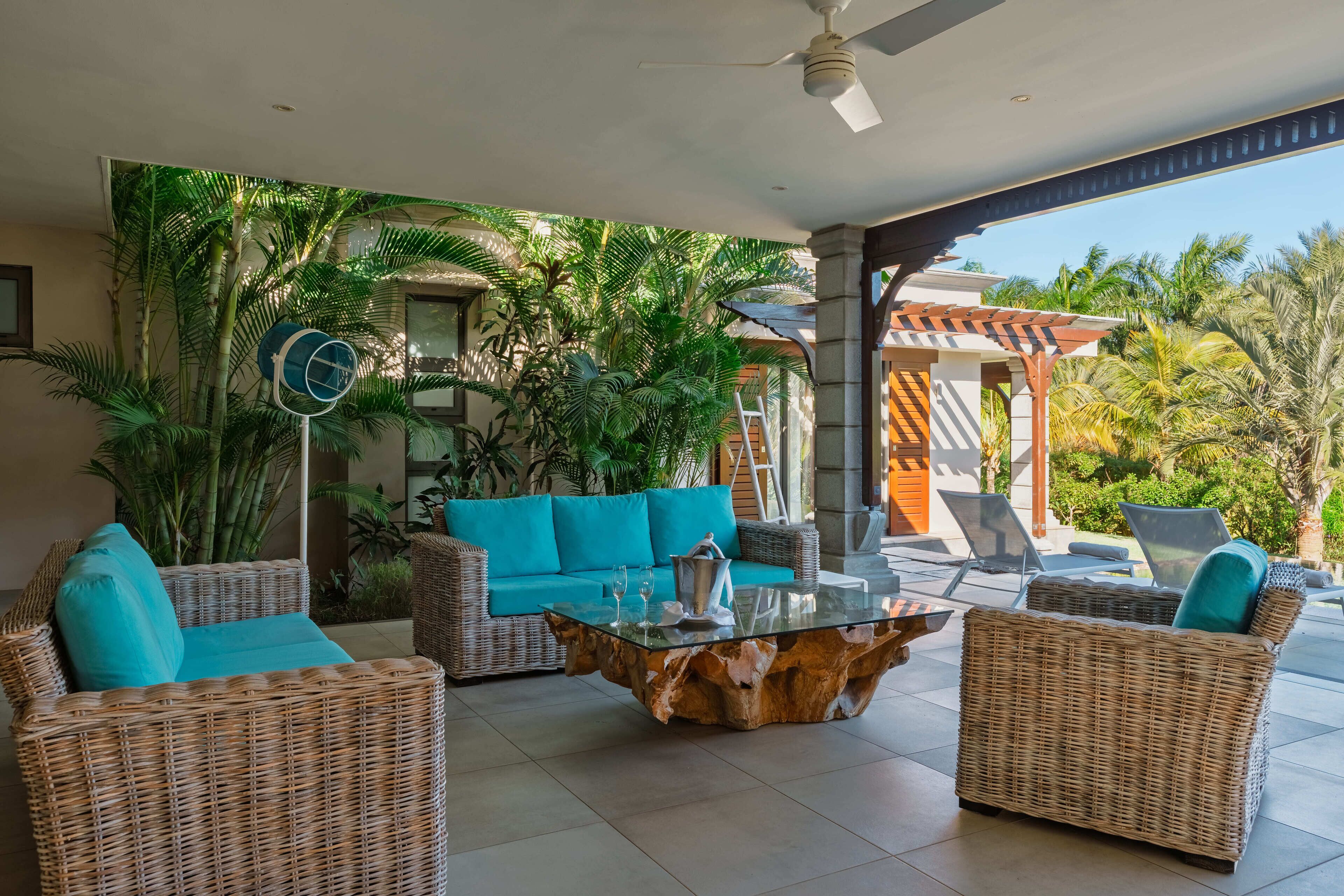 A modern outdoor lounge area with wicker furniture, a glass coffee table, and a view of tropical vegetation.
