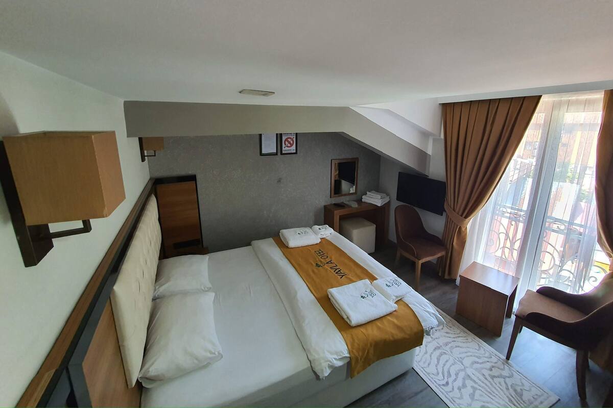 Une chambre d’hôtel avec un lit, un bureau, une chaise, une télévision et une fenêtre avec des rideaux.