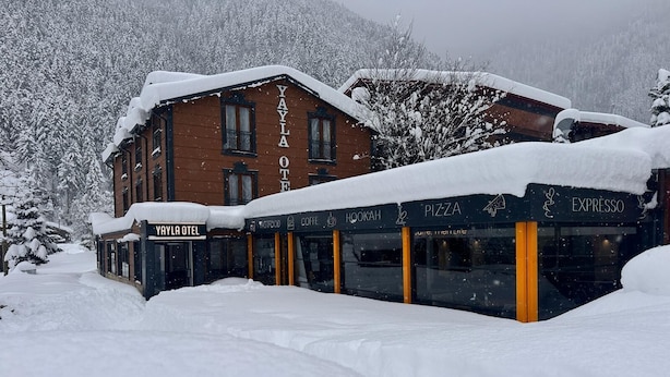 Un edifici cobert de neu amb un cartell que diu 'YAYLA OTEL' i una placa amb 'EXPRESSO' al davant.