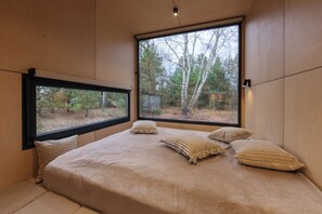 A bedroom with a large window, a bed with striped pillows, and a view of trees outside.