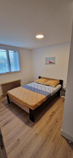 Et soveværelse med en seng, en radiator, et vindue og et billede hængt på væggen.