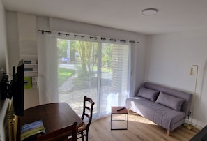 Ein Zimmer mit einem Holztisch, einer grauen Couch und einem Fenster mit transparenten Vorhängen.