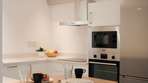 A kitchen with a stainless steel refrigerator, oven, and microwave. There is a breakfast setup with a plate, mug, and glass. - Nila 1 by Huskalia - City Center (Los Llanos de Aridane)