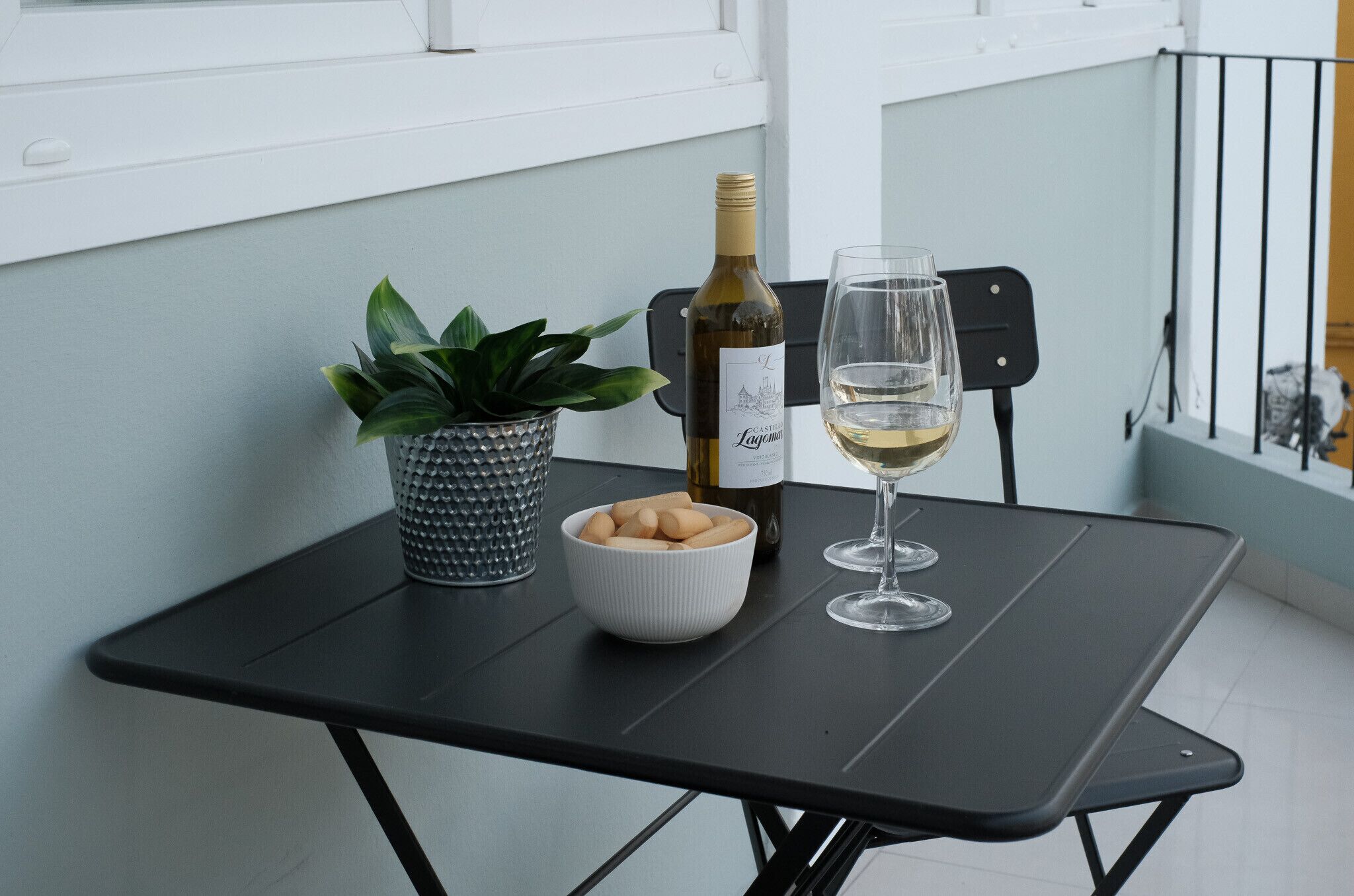A small table with a bottle of wine, a glass, a bowl of cookies, and a potted plant.