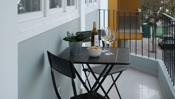 A balcony with a table set for two, featuring a bottle of wine, glasses, a bowl of snacks, and a potted plant. - Nila 1 by Huskalia - City Center (Los Llanos de Aridane)