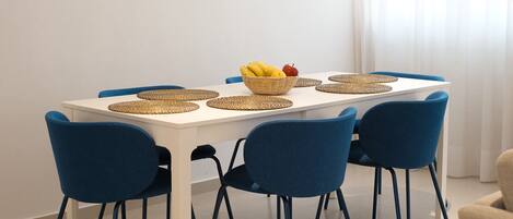 A dining table with a woven placemat, a bowl of fruit, and blue chairs.