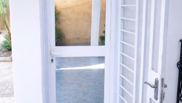 An open white door leading to a courtyard with a concrete floor and a yellow wall.