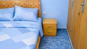A bed with a checkered blue and white bedspread, a wooden headboard, a wooden nightstand with drawers, and a blue tiled floor.