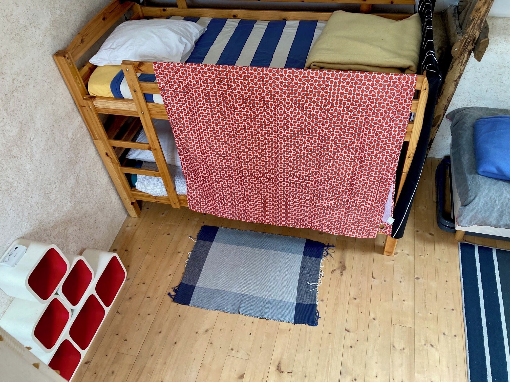 Ein Stockbett mit rotem, gemustertem Bettbezug, einer Holzleiter und einem blau-weiß gestreiften Kissen.