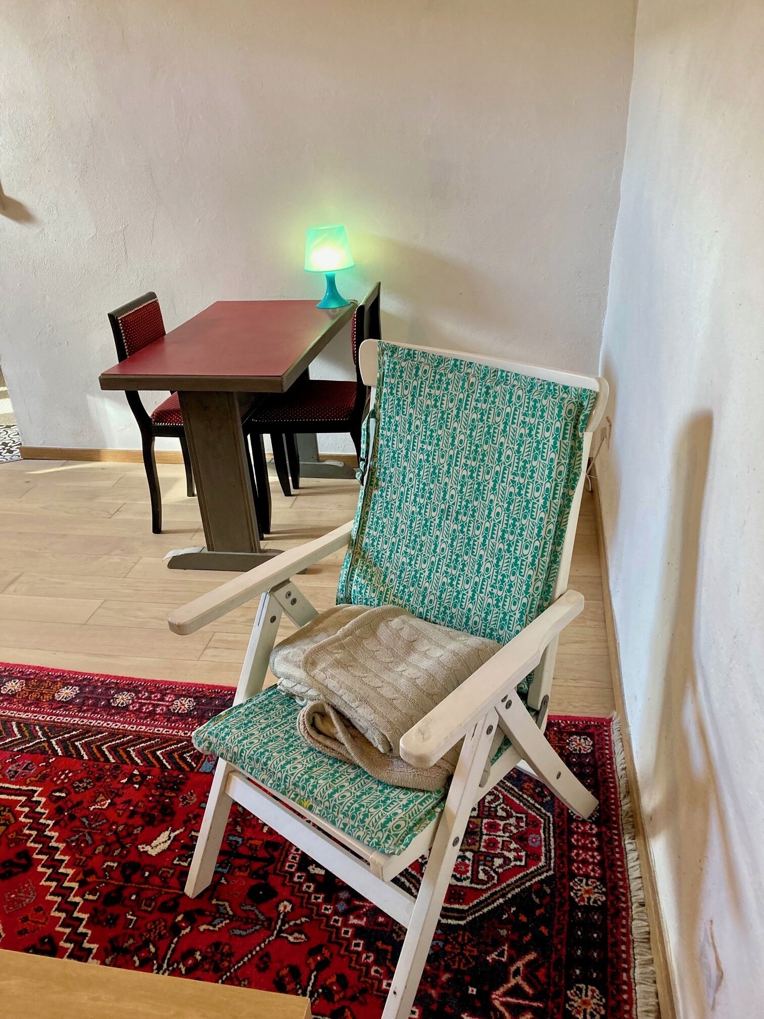 A room with a red table, a green patterned chair, and a red patterned rug.