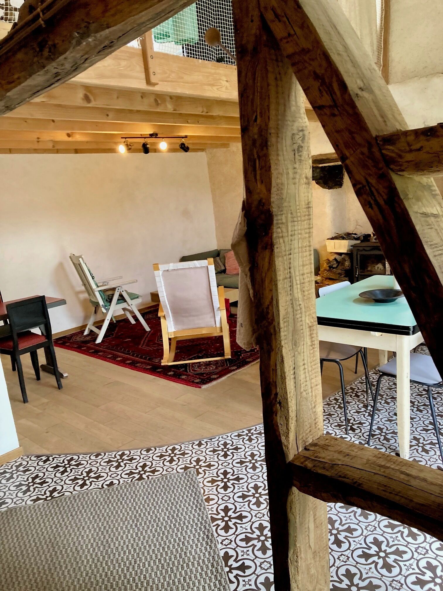 Une pièce rustique avec des poutres apparentes, une table à manger avec des chaises, un tapis à motifs et une petite table sur laquelle se trouve un bol.