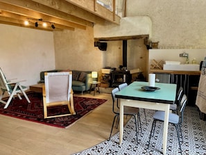A cozy room with a wooden ceiling, a fireplace, a dining table with chairs, a small sofa, and a standing easel. - Gite modulable "Chez Yvette", 65m2 au calme à 800 mètres du centre ville (La Gacilly)