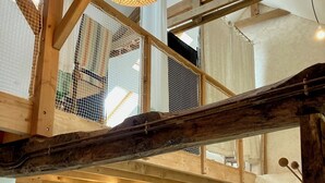 A loft-style room with exposed wooden beams, a hanging light fixture, a view through a mesh window, a sofa, a dining table, and a fireplace. - Gite modulable "Chez Yvette", 65m2 au calme à 800 mètres du centre ville (La Gacilly)