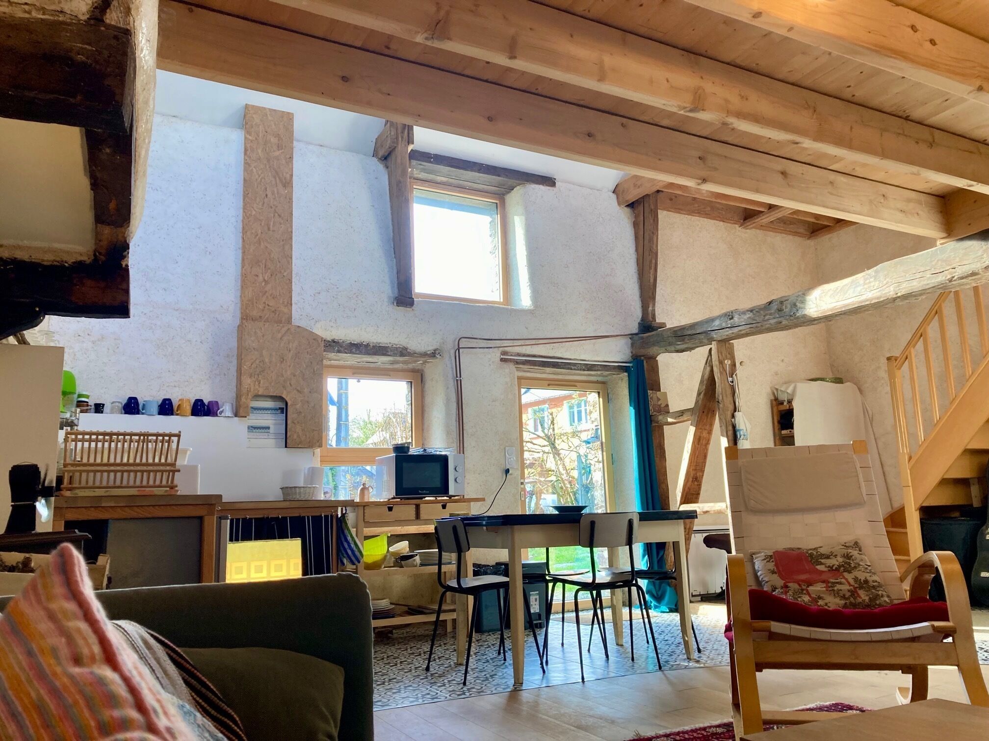 Un ambiente rustico con travi a vista in legno, zona pranzo con sedie e tavolo, divano e una finestra che fa entrare luce naturale.