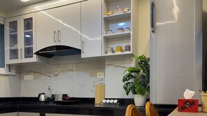 Eine moderne Küche mit weißen Schränken, einer schwarzen Arbeitsplatte, einem Edelstahlkühlschrank und einem Essbereich mit Korbstühlen.