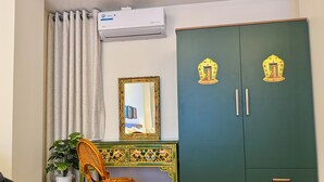 Ein Zimmer mit einem grünen Kleiderschrank, einem Spiegel, einem Korbstuhl und einer Topfpflanze.