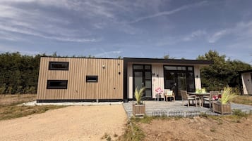 Un bâtiment moderne avec une façade en bois, de grandes fenêtres et un patio aménagé avec du mobilier d’extérieur.