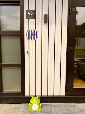 A wooden door with a number plate, a frosted glass window, and a frog decoration on the ground. - Lodge 45 | Luxe lodge met airco | Zennewijnen, Betuwe (Zennewijnen)