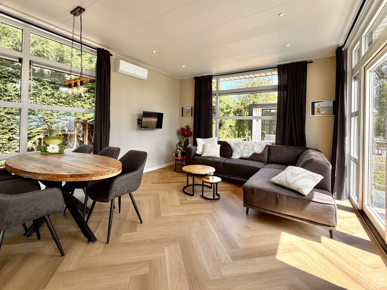 Un salon moderne avec une table à manger ronde en bois, deux canapés et un téléviseur fixé au mur.