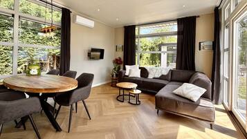 Un salon moderne avec une table à manger ronde en bois, deux canapés et un téléviseur fixé au mur.