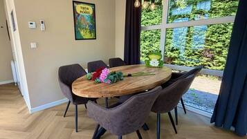 Un coin repas avec une table ronde en bois, six chaises et une vue sur la verdure grâce à de grandes fenêtres.