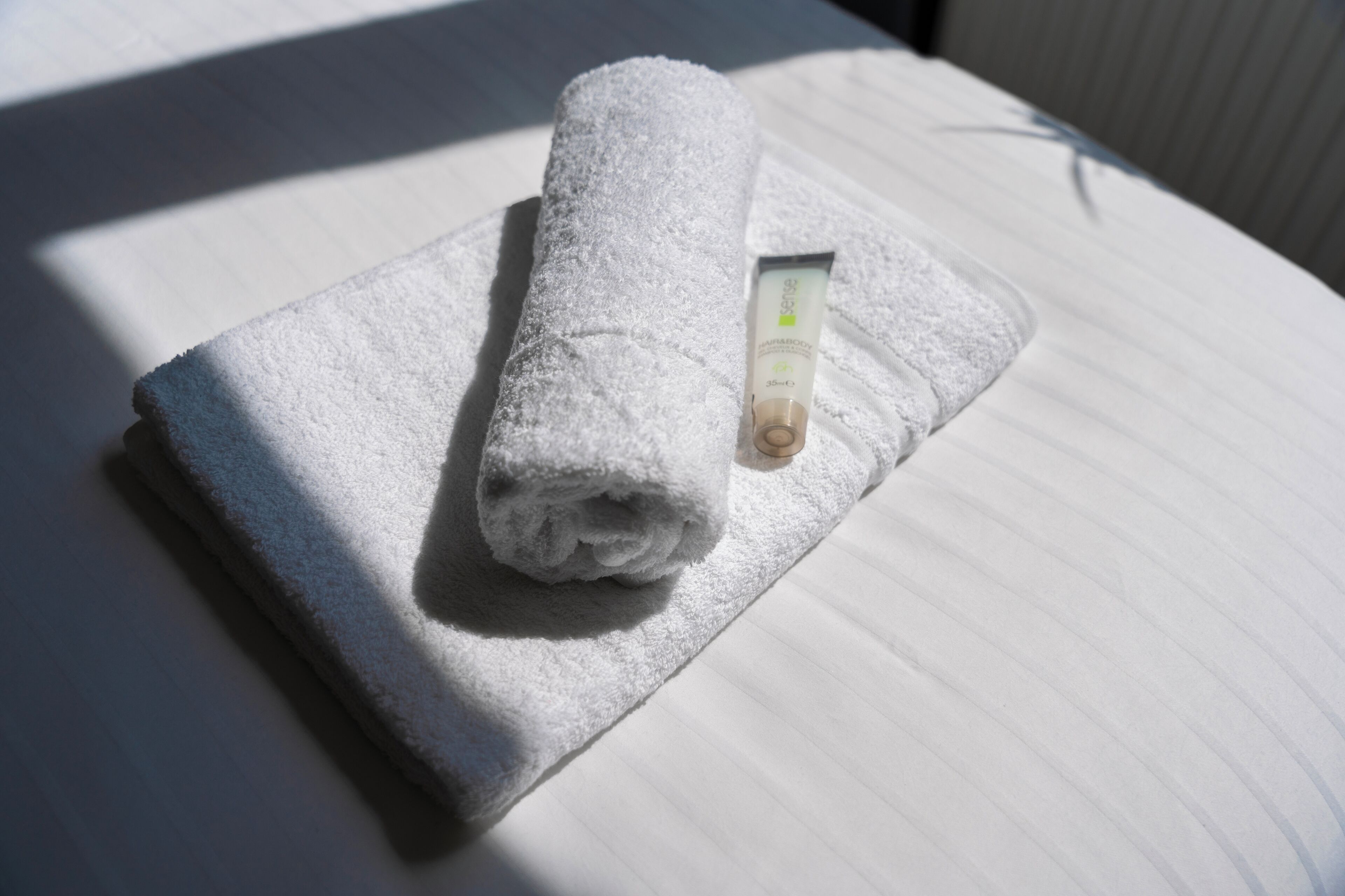 Un asciugamano bianco ordinatamente piegato con una tubetto di crema su un letto con un cuscino a righe.