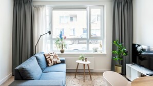 Un salon moderne avec un canapé gris, une table basse ronde, une baignoire blanche et une grande fenêtre avec des rideaux.