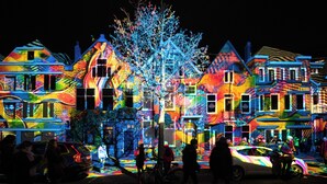 Une rue bordée d’immeubles aux couleurs vives, illuminés, avec un arbre au centre.