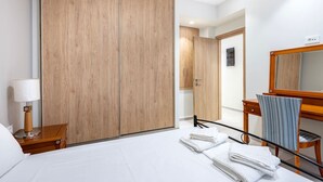 A hotel room with a large bed, a wooden wardrobe, a desk with a chair, a lamp, and a mirror.