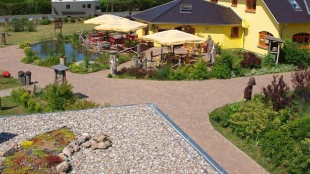 A yellow building with a dark roof, outdoor seating, a pond, and a gravel area with rocks. - Landhotel zum Honigdieb (Ribnitz-Damgarten)