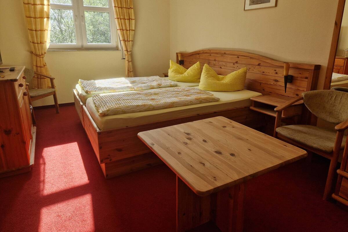 Une chambre avec deux lits, un bureau en bois, une chaise et une fenêtre avec des rideaux.