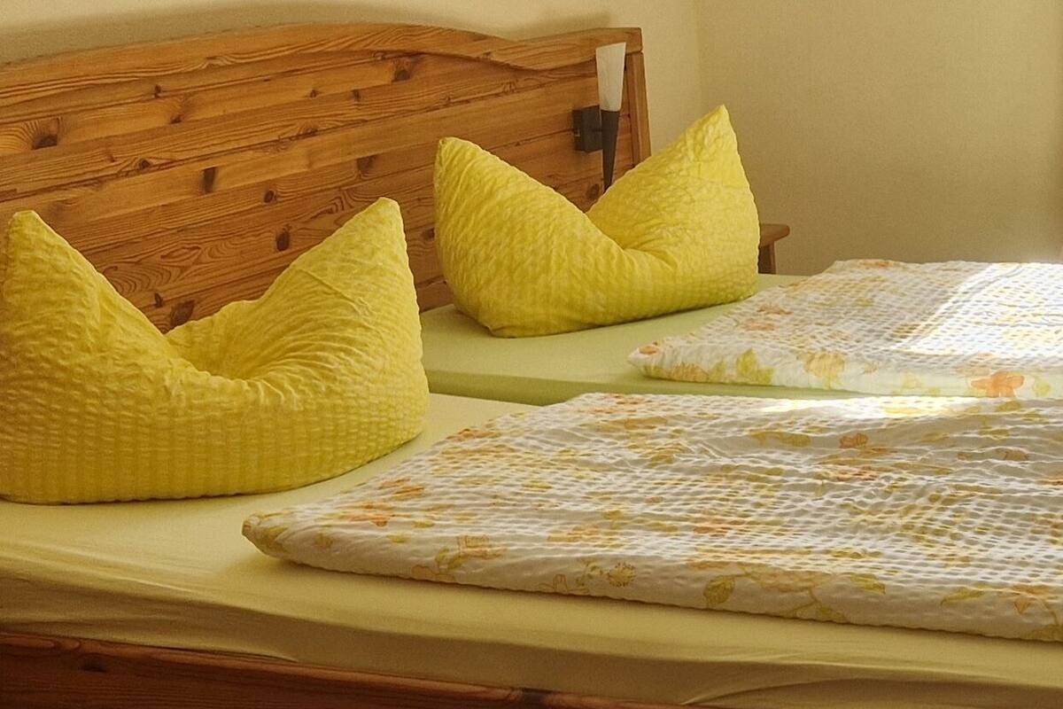 Un lit avec une tête de lit en bois, deux oreillers jaunes et une couvre-lit à motifs floraux.
